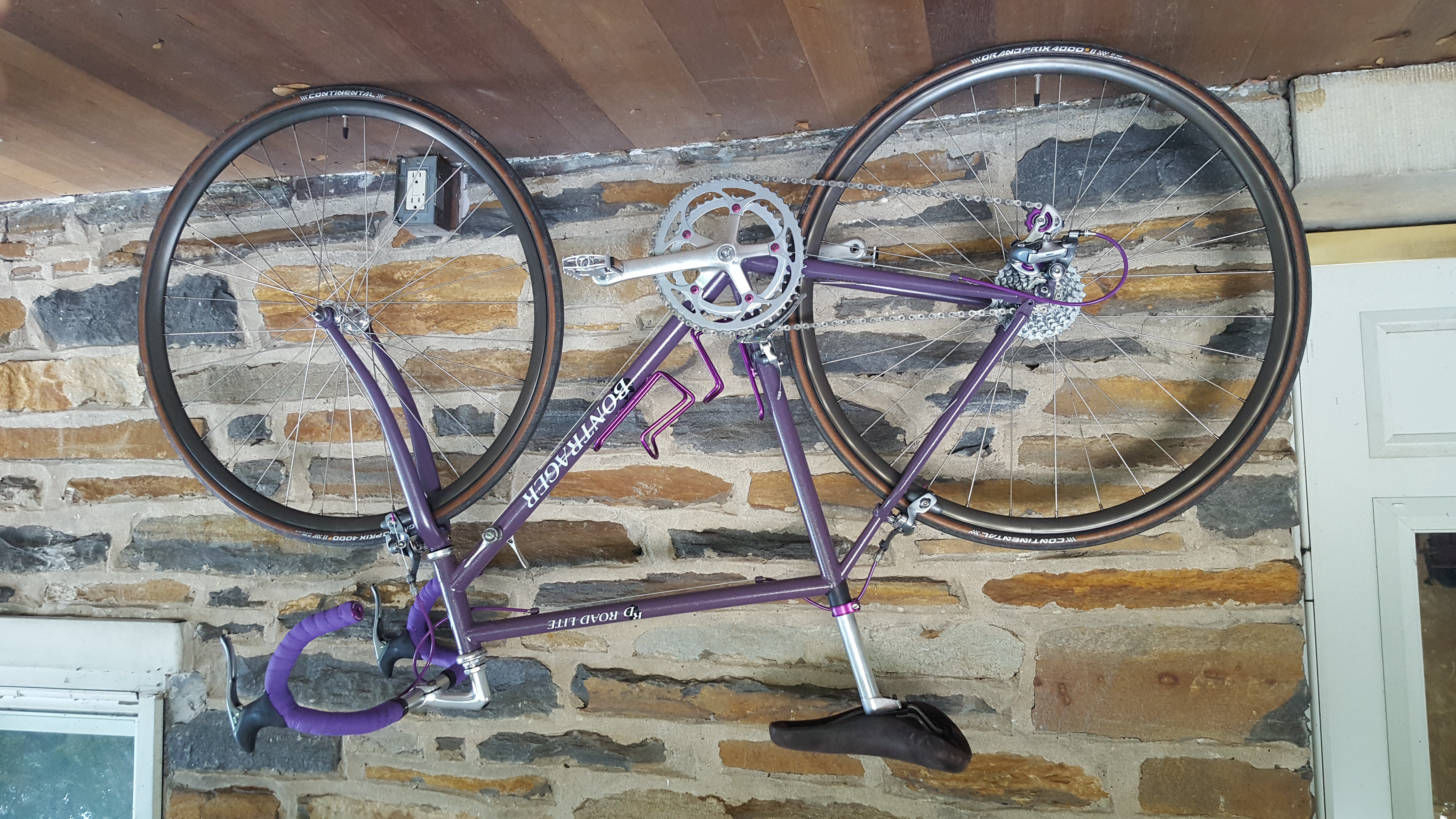 A purple bicycle posed against a stone wall. Purple derailleur wheels and crank bolts are visible.